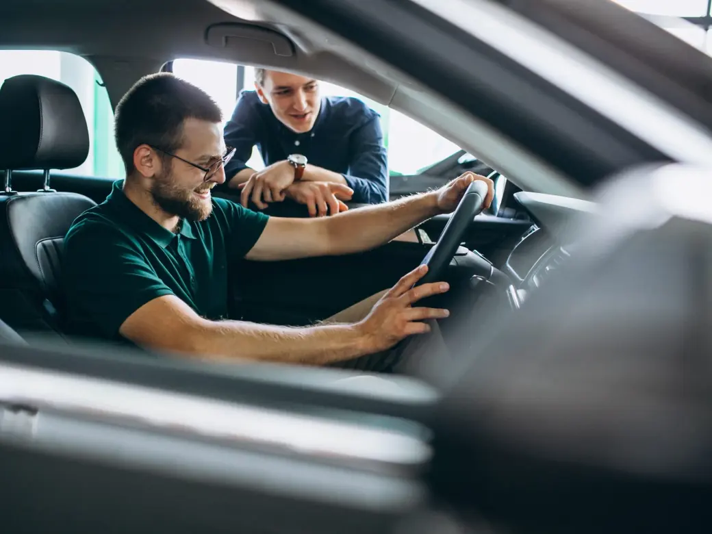 Homem sorrindo ao volante de um carro enquanto conversa com um consultor